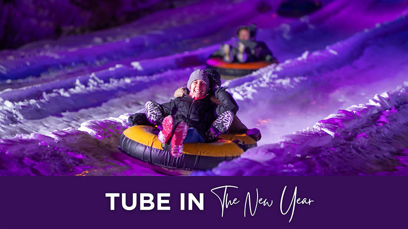 Nighttime photo of people snow tubing down a glowing purple-lit slope with the caption ‘Tube in the New Year.’