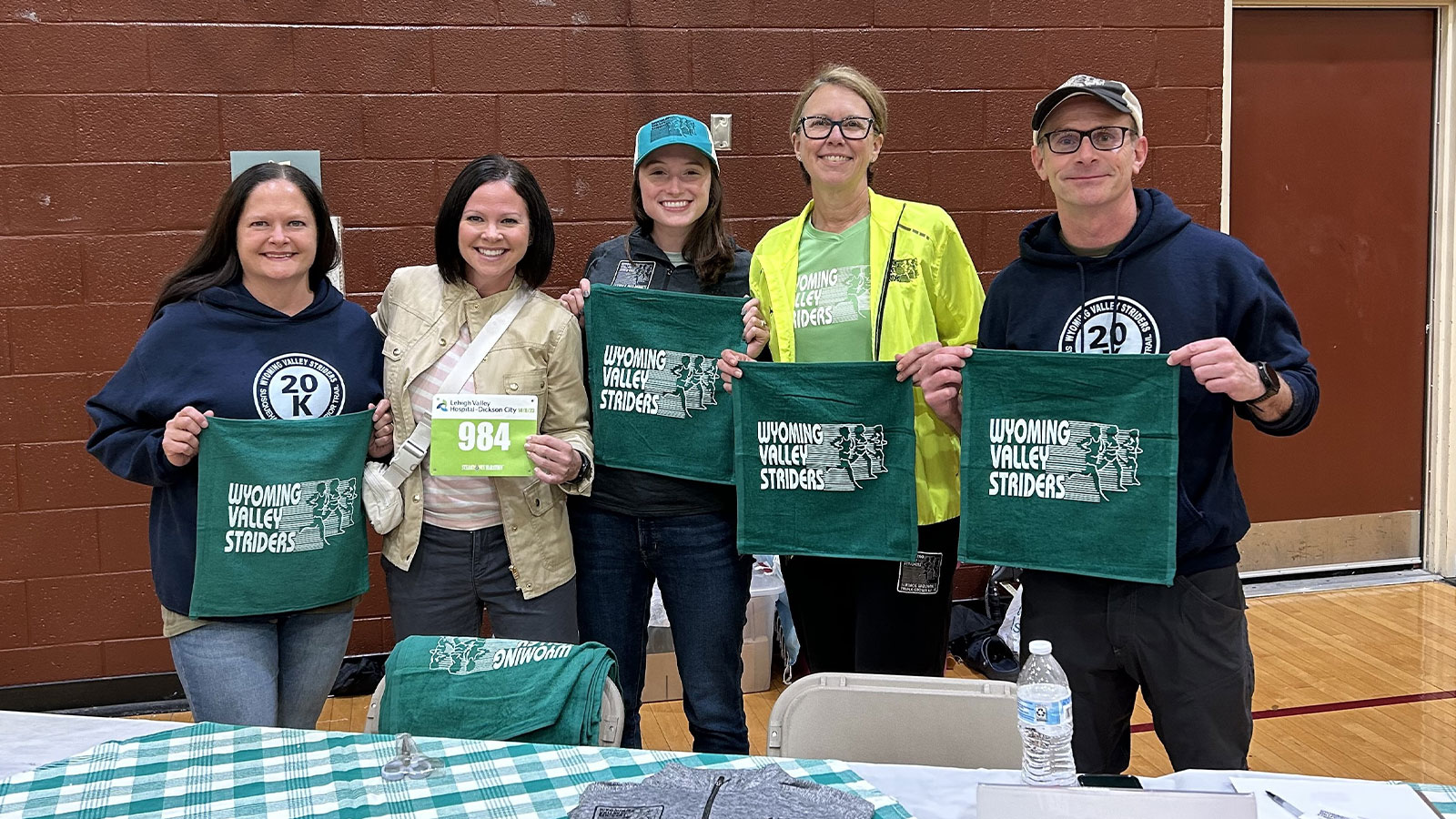 Wyoming Valley Striders board members smile and hold club towels while volunteering at a race expo table.
