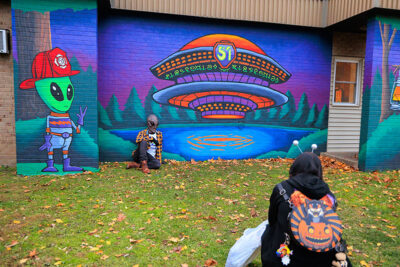 A man dressed as an alien gets his photo taken in front of a spaceship mural at the second annual Carbondalien Festival in Carbondale, PA.