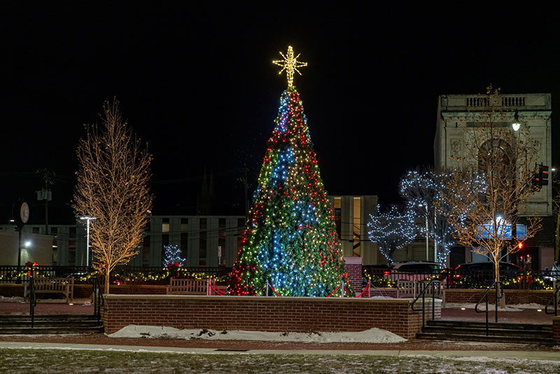 A brightly lit Christmas tree glows in a snowy downtown plaza during the CAN DO Community Christmas celebration in Hazleton, PA.