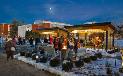 People enjoying a warm fire while standing in line to meet Santa under a moonlit sky during the Merry and Bright event at Marywood University in Scranton, PA.
