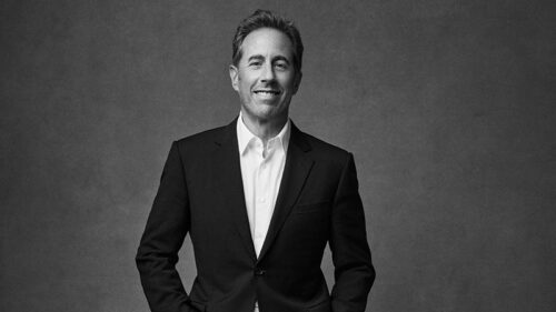 Black-and-white portrait of Jerry Seinfeld wearing a suit jacket and smiling, appearing at the F.M. Kirby Center in Wilkes-Barre, PA.