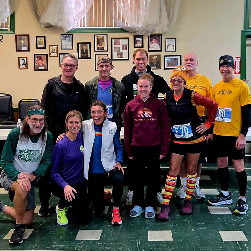 Wyoming Valley Striders members gather indoors after Run for the Diamonds, smiling and celebrating together in race attire and medals.