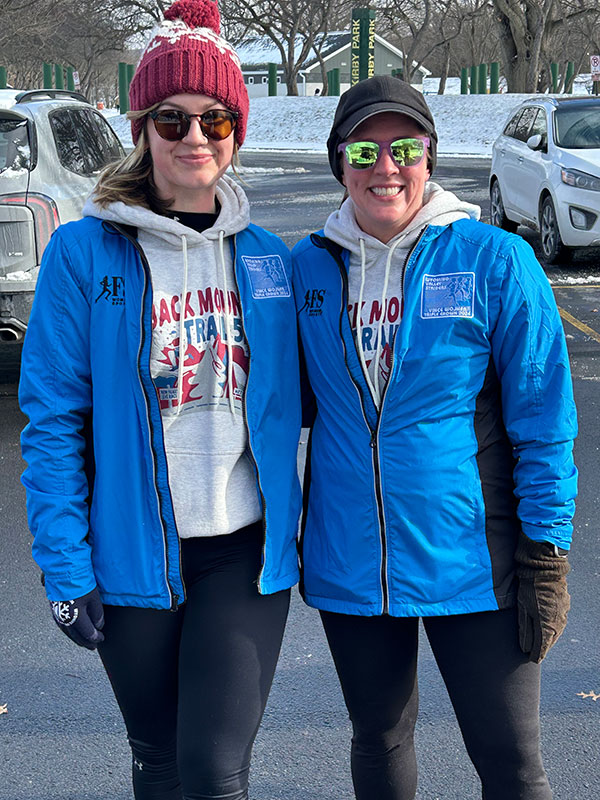 Two Wyoming Valley Striders members stand side by side wearing blue jackets and winter gear at Kirby Park during the New Year’s Day social run.