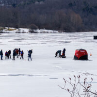 People ice fishing and walking across a frozen lake during Winterfest at Lackawanna State Park in North Abington Township, PA.