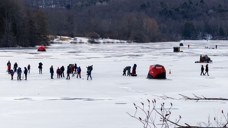 People ice fishing and walking across a frozen lake during Winterfest at Lackawanna State Park in North Abington Township, PA.