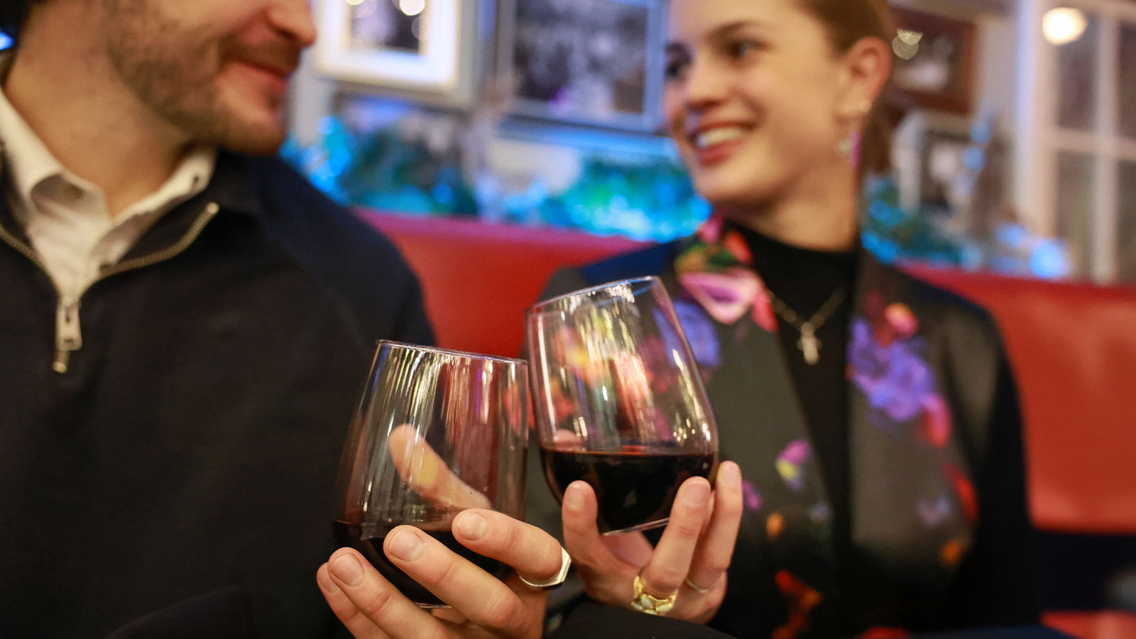 Two people sit at a restaurant booth holding glasses of red wine and smiling at each other at Abbiocco in Clarks Summit, PA.