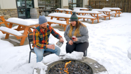 A pair sitting on a snowy patio in front of a fire pit drinking beer at Wallenpaupack Brewing Company