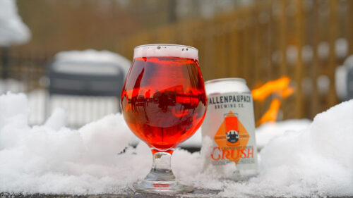 A glass of Cranberry Orange Crush next to a can on a snowy patio fireplace