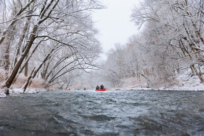A wide view of the Lackawanna River with freshly fallen snow on the surrounding trees as a canoe makes it way down stream during Shiverfest in Scranton, PA.