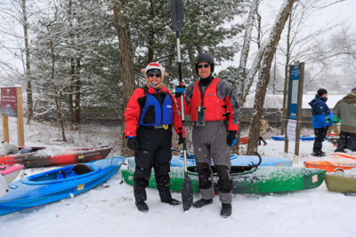 Two people pose for the camera while holding their oars next to their kayaks during Shiverfest in Scranton, PA.