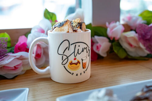 A mug featuring Slims Cafe logo in Freeland, PA, is filled with hot chocolate and topped with whipped cream.