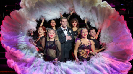 The cast of Chicago the musical, ahead of their visit hosted by Broadway Theatre League, is surrounded by white feathers on stage.