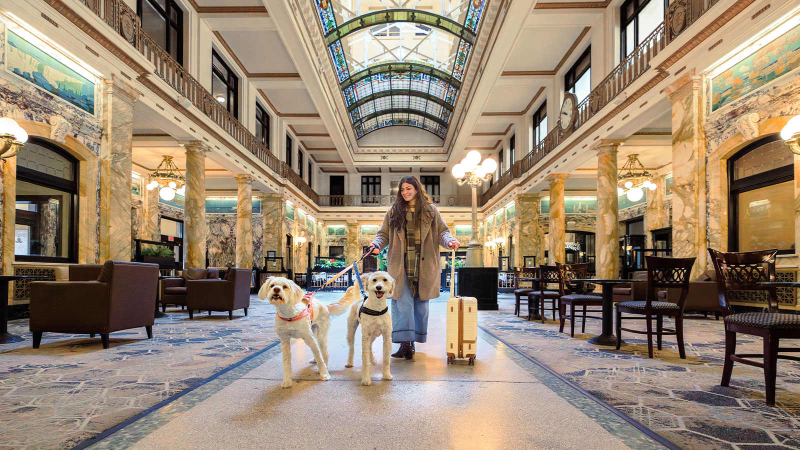 A woman with a suitcase walks her two dogs through the lobby of the Radisson Lackawanna Station Hotel, a pet-friendly hotel in Scranton, PA.