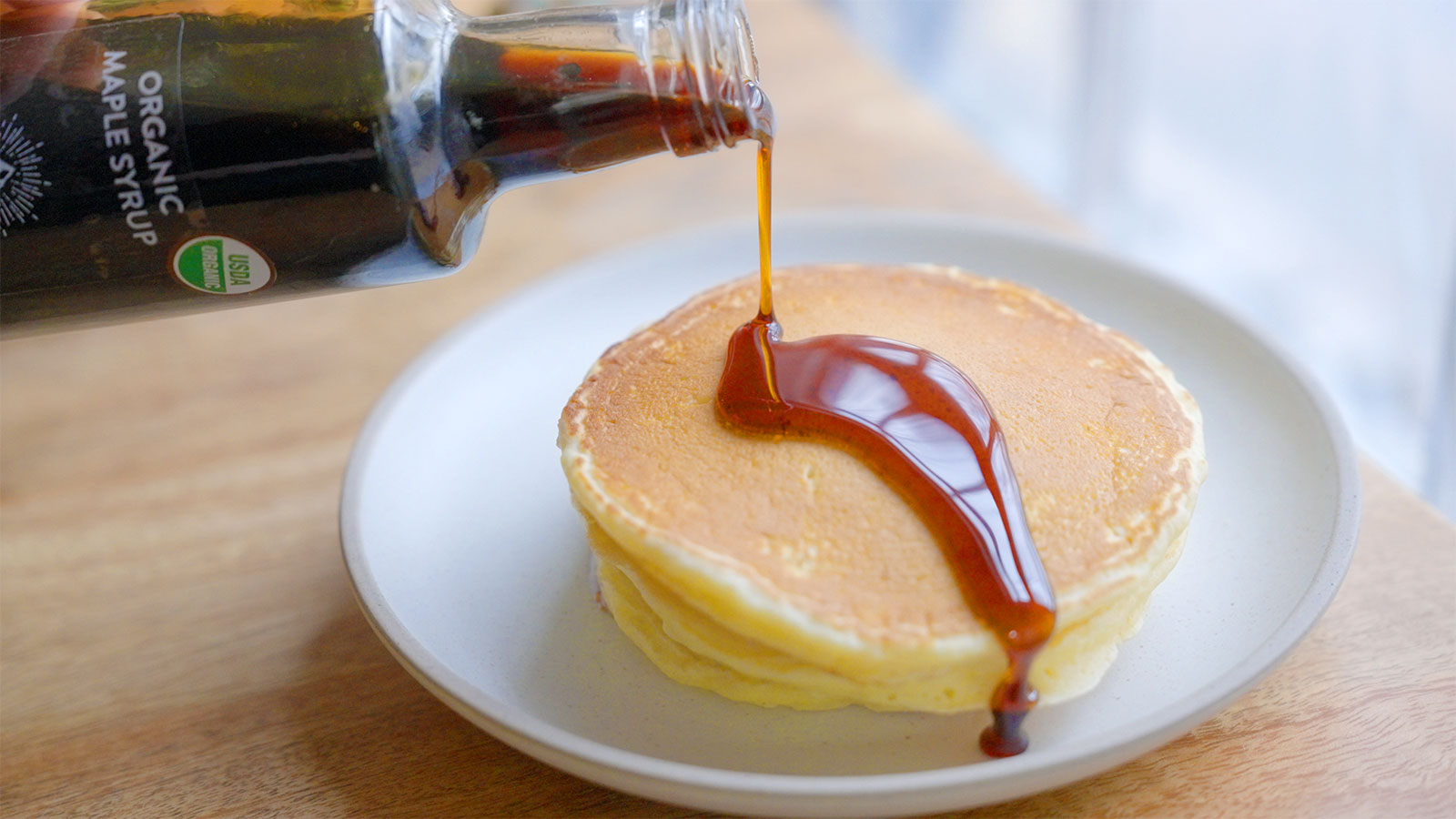 Maple Syrup from Pocono Mountain Maple in Newfoundland, PA being poured over a stack of pancakes.