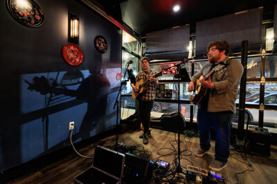 Two men perform acoustic guitars on a small stage inside a venue during Celebrate Music in Pittston, PA.