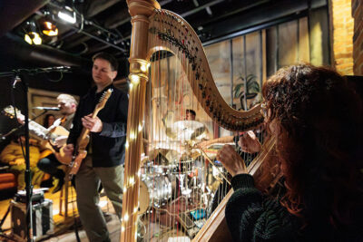 Musicians perform on stage with guitar, drums and harp during Celebrate Music in Pittston, PA.