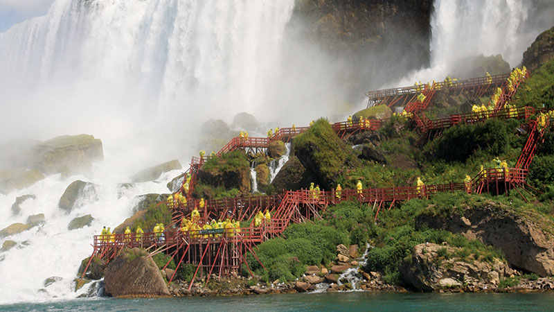 People climbing the many stairs to get closer to a waterfall at Niagara Falls.