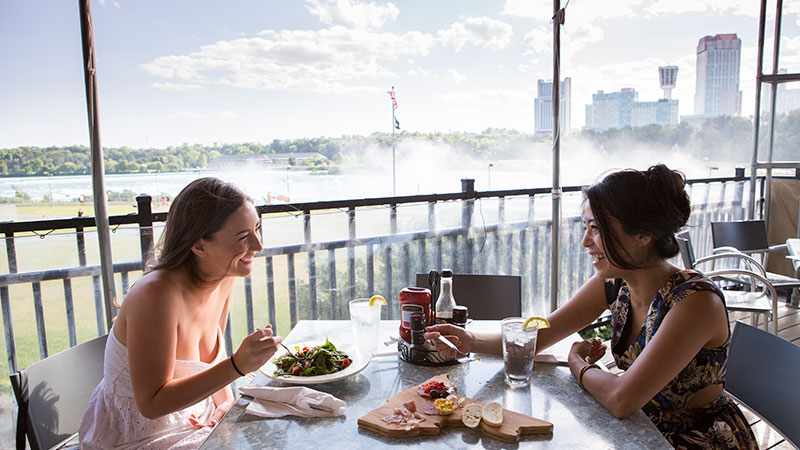 Two women dining with the scenic falls in the background at Top of The Falls restaurant in Niagara Falls.