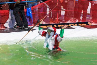 A skier dressed as Santa Claus carries his skies while treading through water at Mountainfest at Montage Mountain in Moosic, PA.