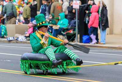 A man dress as a leprechaun with an oar in his hand sits in an inflatable tube on wheels that's being pulled by vehicle during the St. Patrick's Day parade in Scranton, PA.