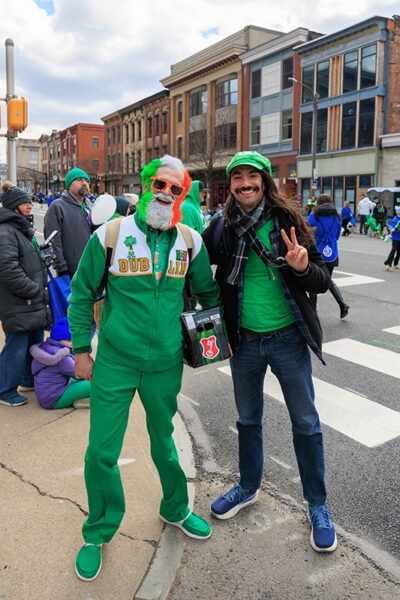 A man with orange, white and green painted in his hair, face and beard stands next to a guy in green Luigi hat during the St. Patrick's Day parade in Scranton, PA.