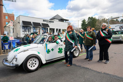A man gives a thumbs up to the camera while cruising down the parade route in a white punch bug convertible during Scranton's St. Patrick's Day parade.