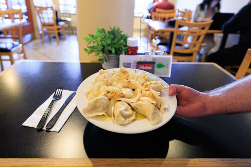 A close-up of a servers hand placing down a plate of buttery pierogies on a table a the Pierce Street Deli in Kingston, PA.