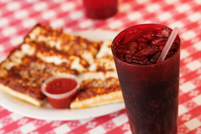 A pepsi sits in red plastic put on a red and white checkered tablecloth with cheesy breadsticks in the background at Pizza Hut Classic in Tunkhannock, PA.