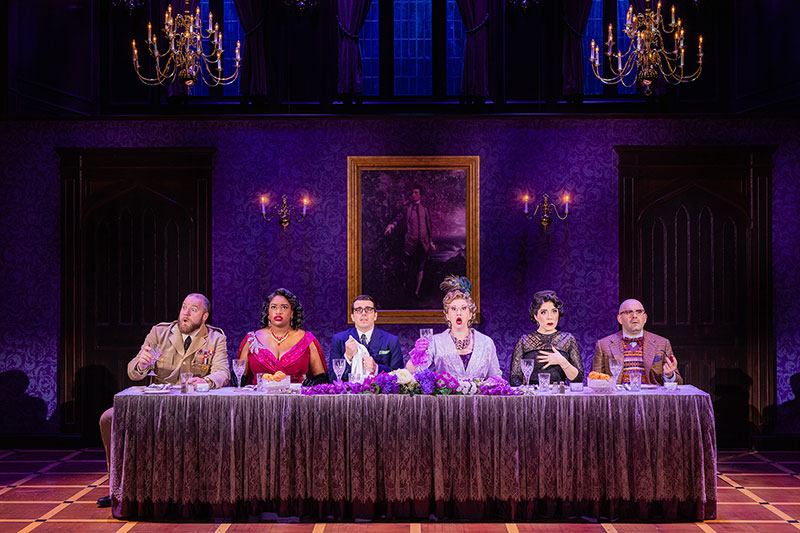 The cast of CLUE the musical, presented by Broadway Theatre League in Scranton, PA, sits at a dining table on stage.